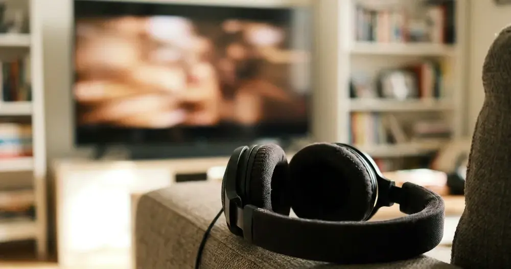 fones de ouvido sobre o braço de um sofá com televisão desfocada ao fundo
