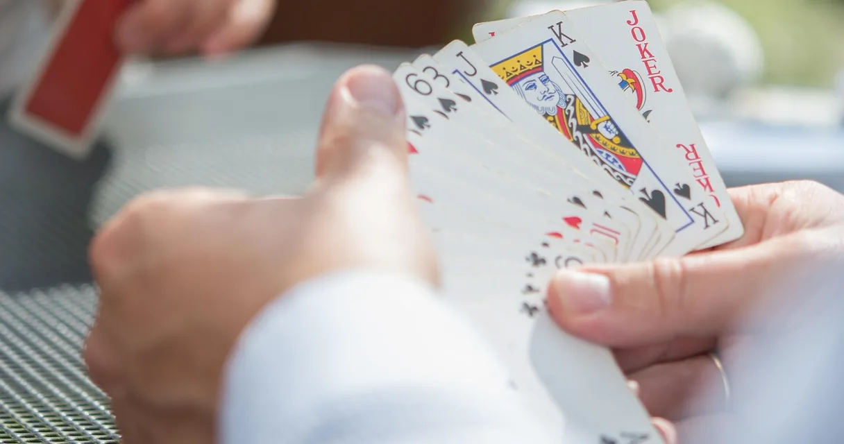 Mão segurando um leque de cartas de baralho, ilustrando como jogar buraco
