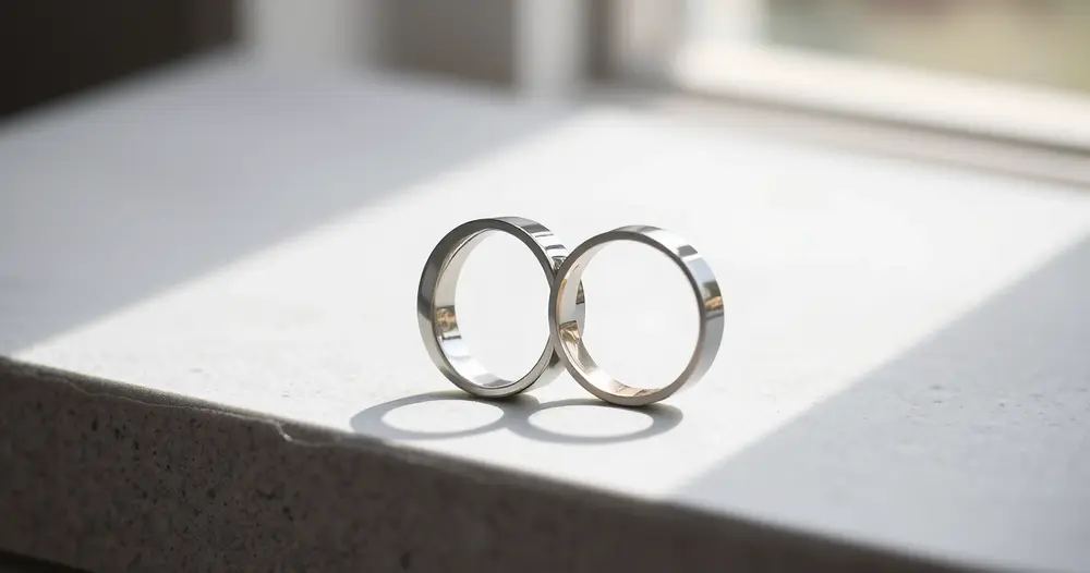 Duas alianças lisas lado a lado sobre superfície de pedra cinza clara com luz suave de janela