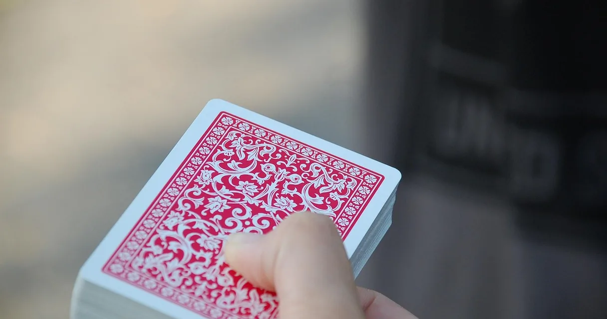 Mão segurando um baralho de cartas com verso estampado, ilustrando truco paulista e truco mineiro